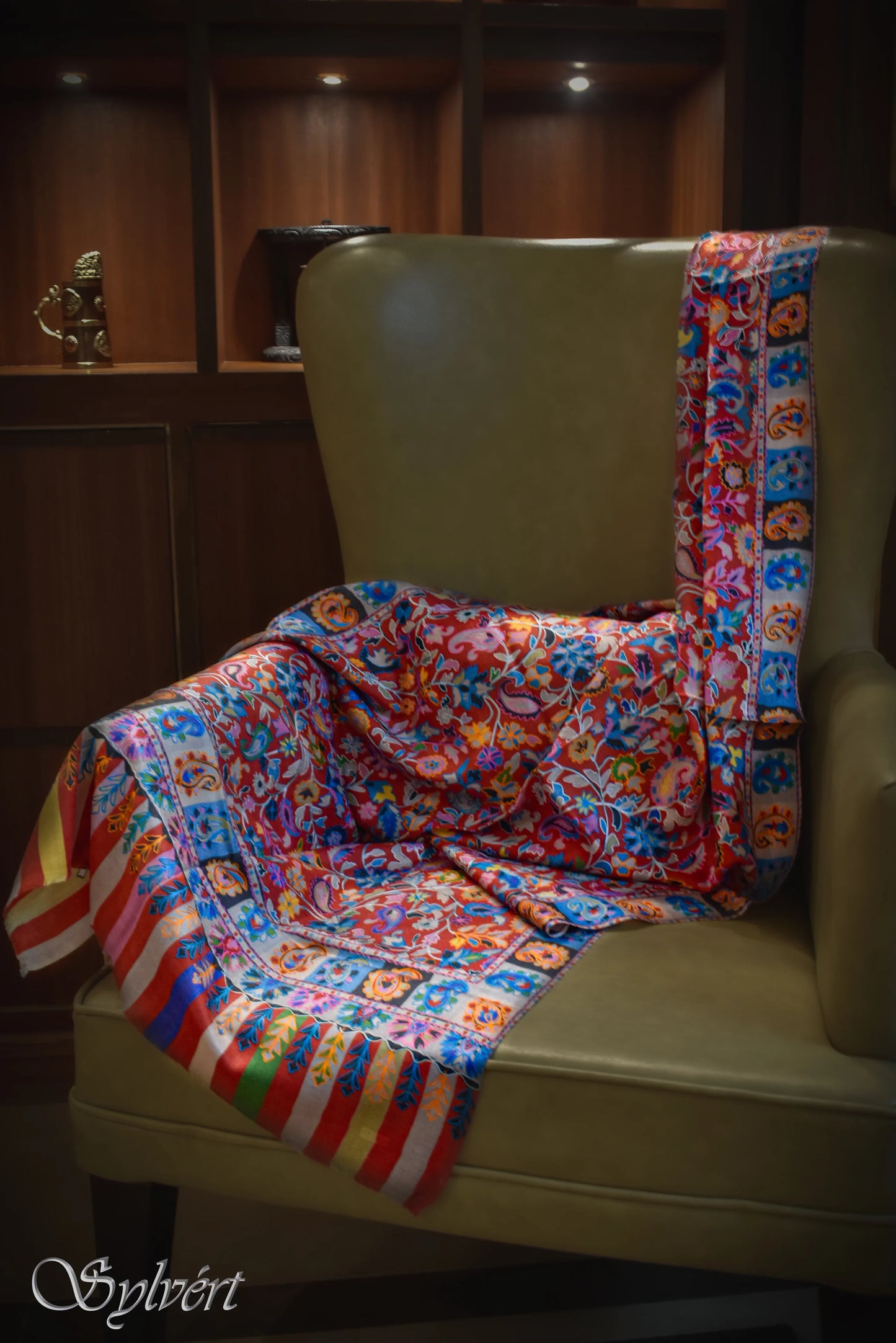 Colorful patterned textile draped over olive green armchair in cozy wooden room