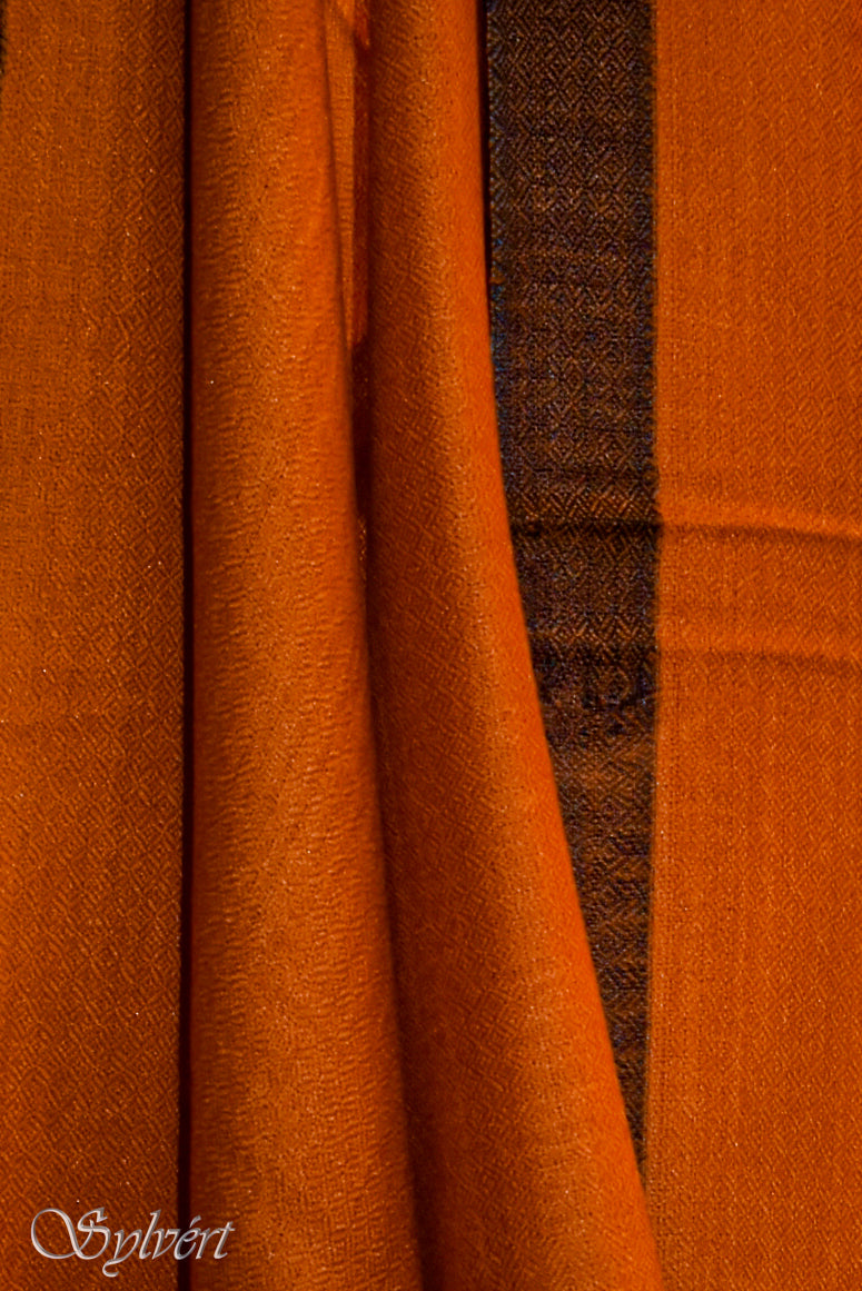 Close up draped image of a orange and black bordered Rivesto cashmere stole from Sylvért's Rivanor collection