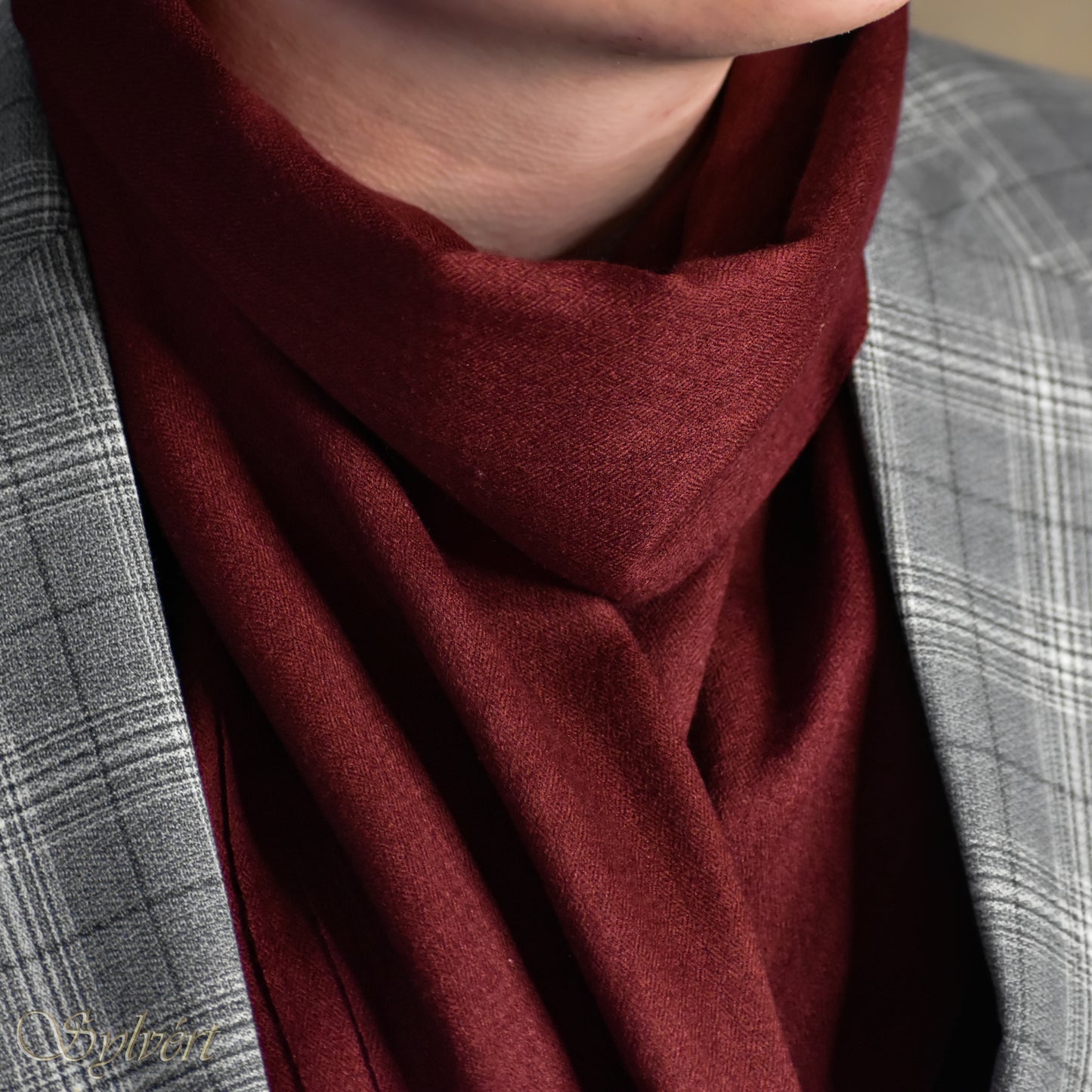 A styled shot of a maroon cashmere Rivella Morven scarf from Sylvért's Rivanor collection worn under a grey plaid blazer