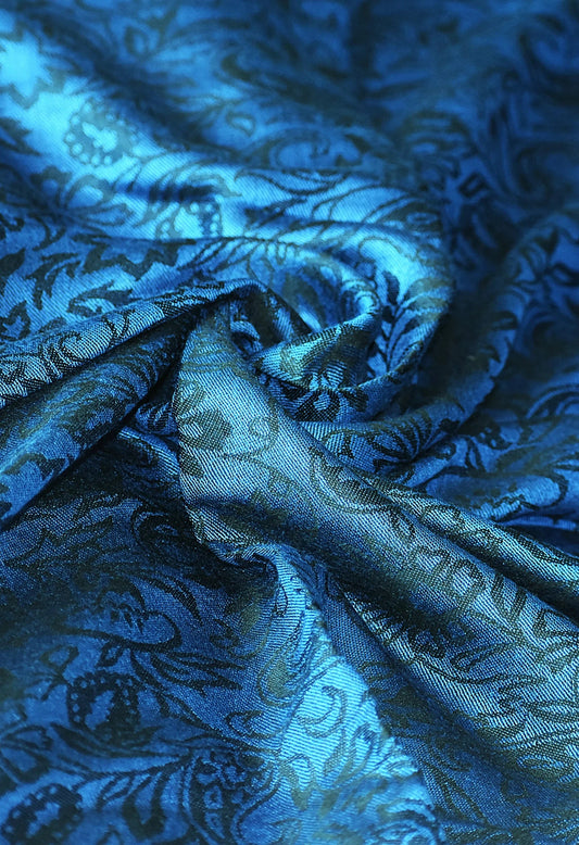 Close-up of shiny blue fabric with intricate floral brocade pattern and soft folds