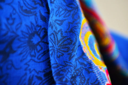 Close-up of vibrant blue fabric with intricate black floral print and colorful embroidery