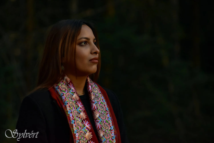 Portrait of woman with long brown hair wearing a colorful embroidered scarf against dark blurred background