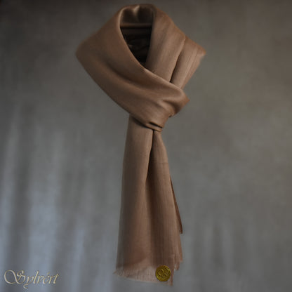 A natural "blush" cashmere Rivella Relor Scarf from Sylvért's Rivanor Collection. looped and threaded, suspended in the air in front of a beige background showing the Sylvért Stamp
