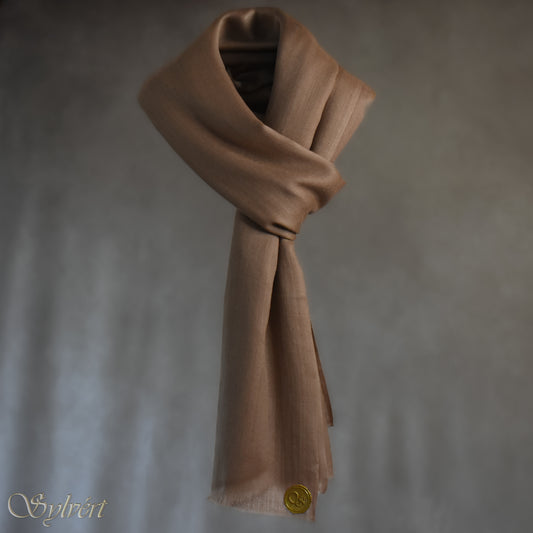 A natural "blush" cashmere Rivella Relor Scarf from Sylvért's Rivanor Collection. looped and threaded, suspended in the air in front of a beige background showing the Sylvért Stamp