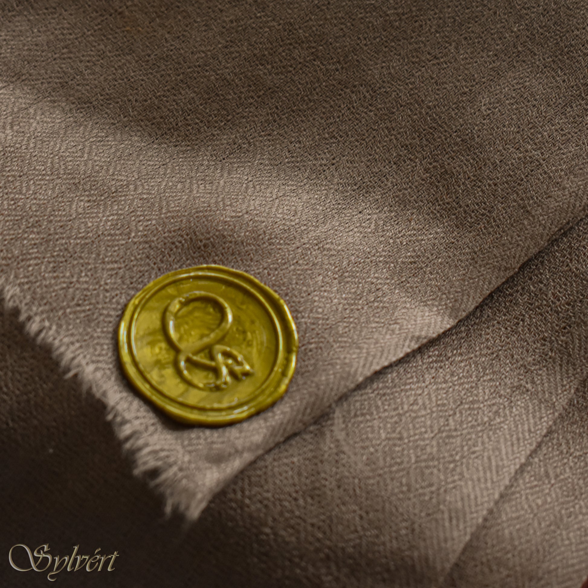 A natural "blush" cashmere Rivella Relor Scarf from Sylvért's Rivanor Collection, showing gold Sylvért stamp. Folded to show the texture.