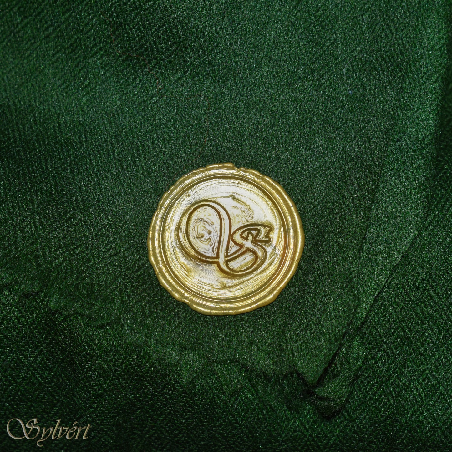 A green cashmere Rivella Tavon Scarf from Sylvért's Rivanor Collection, folded to show the diamond weave texture and the gold Sylvért stamp