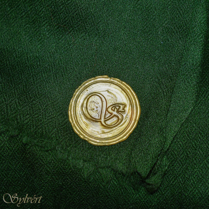 A green cashmere Rivella Tavon Scarf from Sylvért's Rivanor Collection, folded to show the diamond weave texture and the gold Sylvért stamp