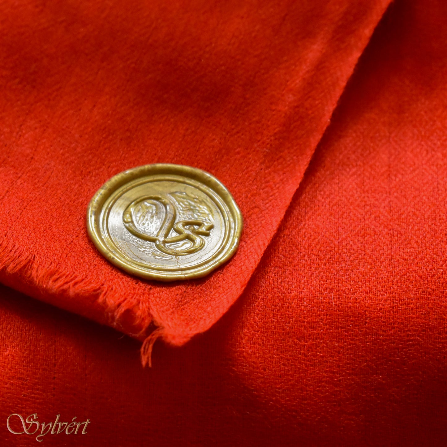 A red cashmere Rivella Sirel Scarf from Sylvért's Rivanor Collection, folded to show the diamond weave texture and the gold Sylvért stamp