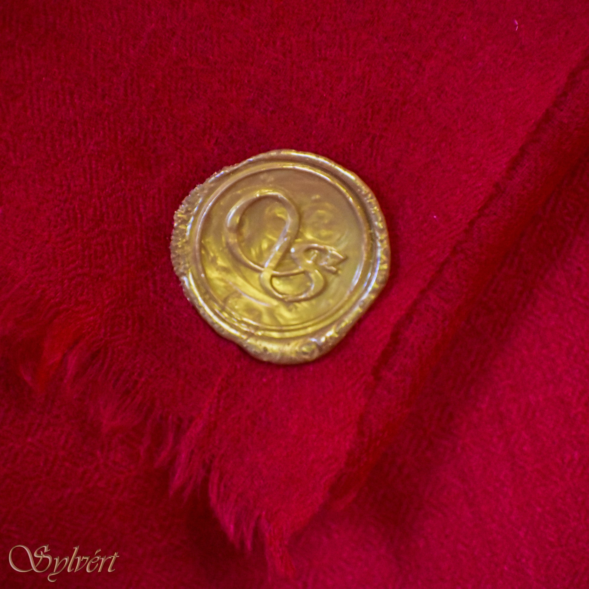 A red Corvella Sorell from Sylvért's Coronis collection, folded to show the diamond weave texture  and gold Sylvért stamp