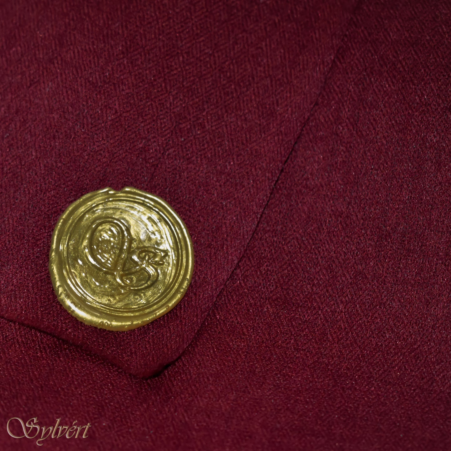A maroon cashmere Rivella Morven Scarf from Sylvért's Rivanor Collection, folded to show the diamond weave texture and the gold Sylvért stamp