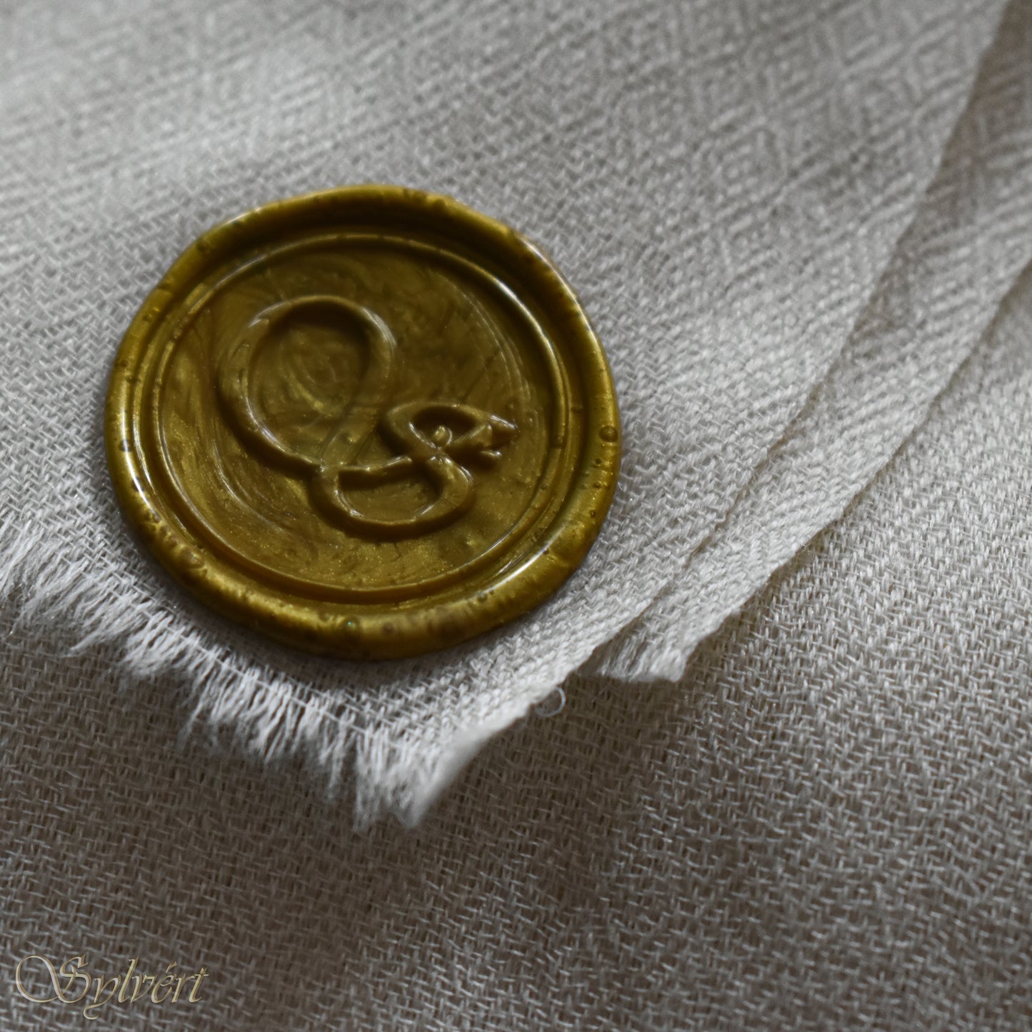 A white cashmere Rivella Caelis Scarf from Sylvért's Rivanor Collection, folded to show the diamond weave texture and the gold Sylvért stamp