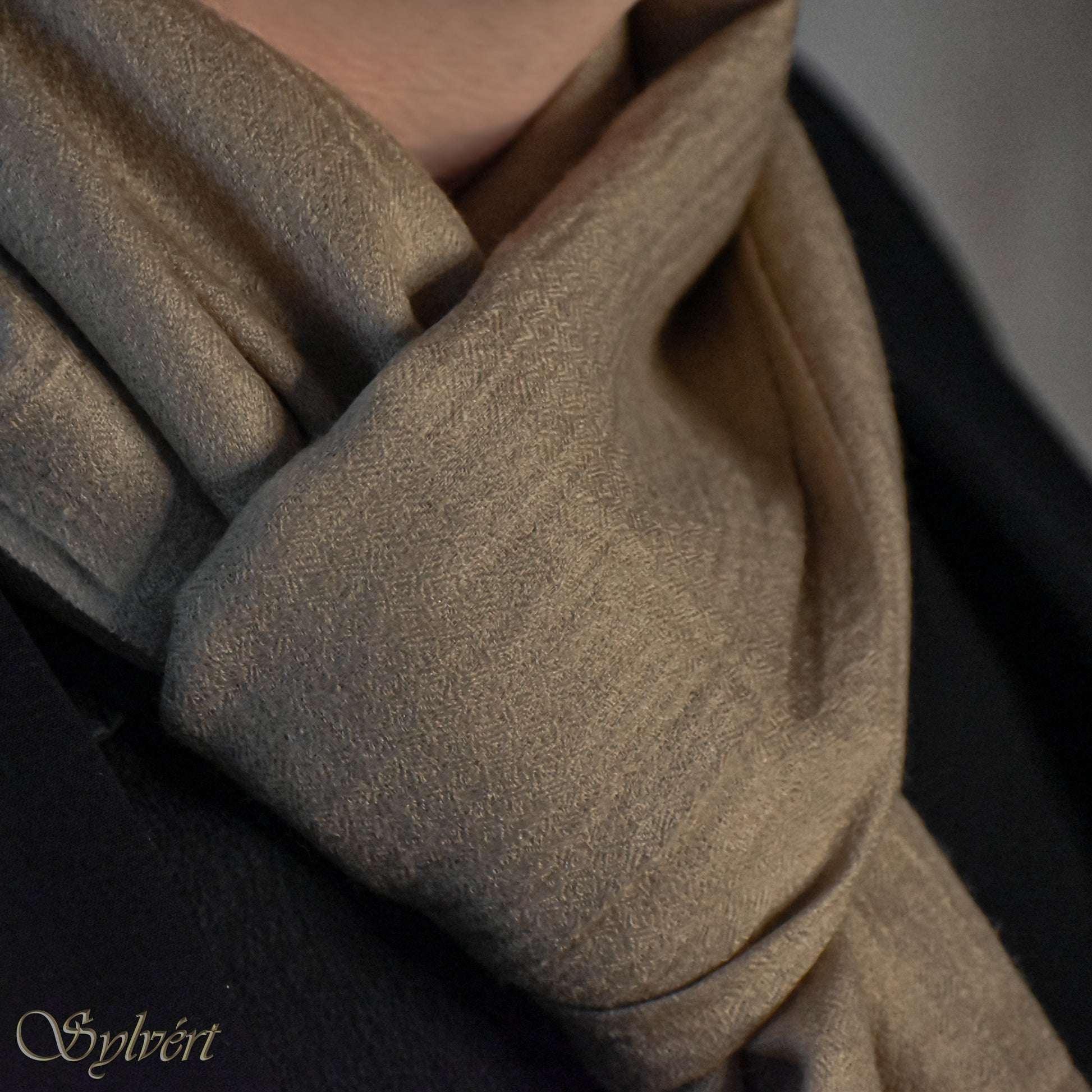 A styled shot of a  beige Corvella Draván from Sylvért's Coronis collection, worn around the neck under a black jacket, showing it's diamond weave texture