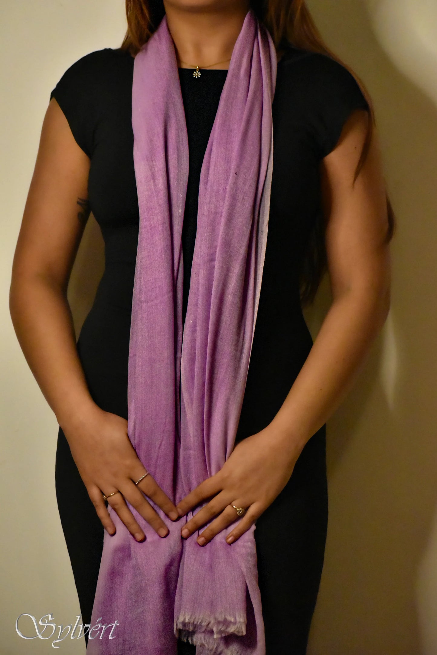 Woman in black dress wearing a long purple scarf against neutral background