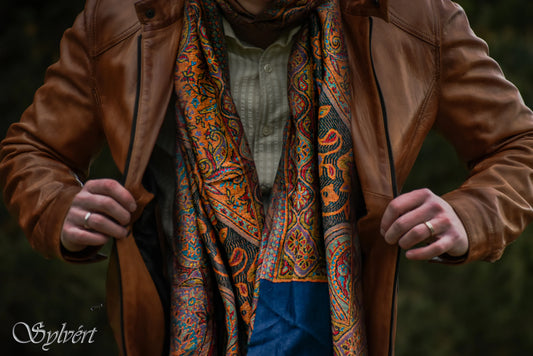 Male model wearing a brown leather jacket and Corvello "Jamawar" full work pashmina with a blue border, from Sylvért's Coronis collection
