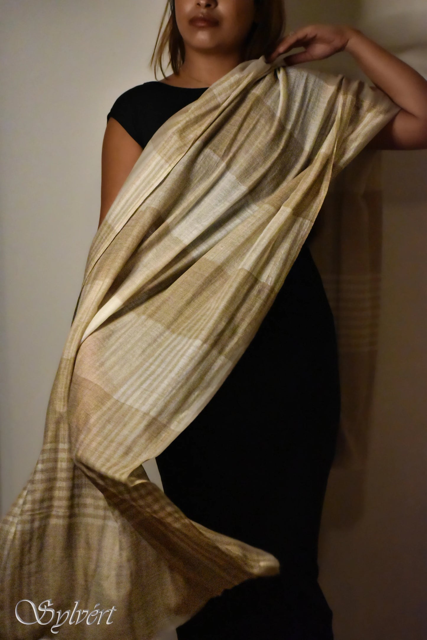 Woman in black dress draping a beige and brown striped shawl indoors