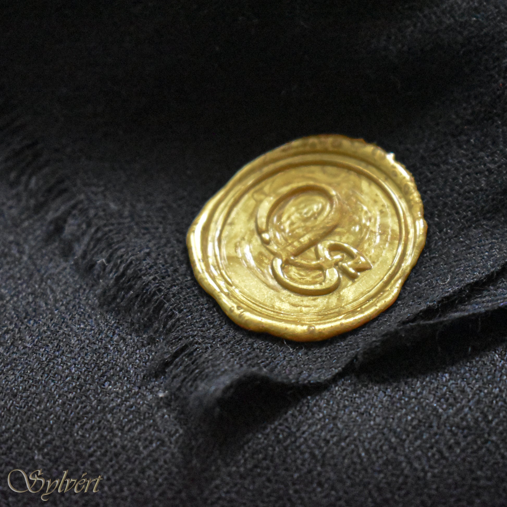 A black cashmere Rivella Velin Scarf from Sylvért's Rivanor Collection, folded to show the diamond weave texture and the gold Sylvért stamp
