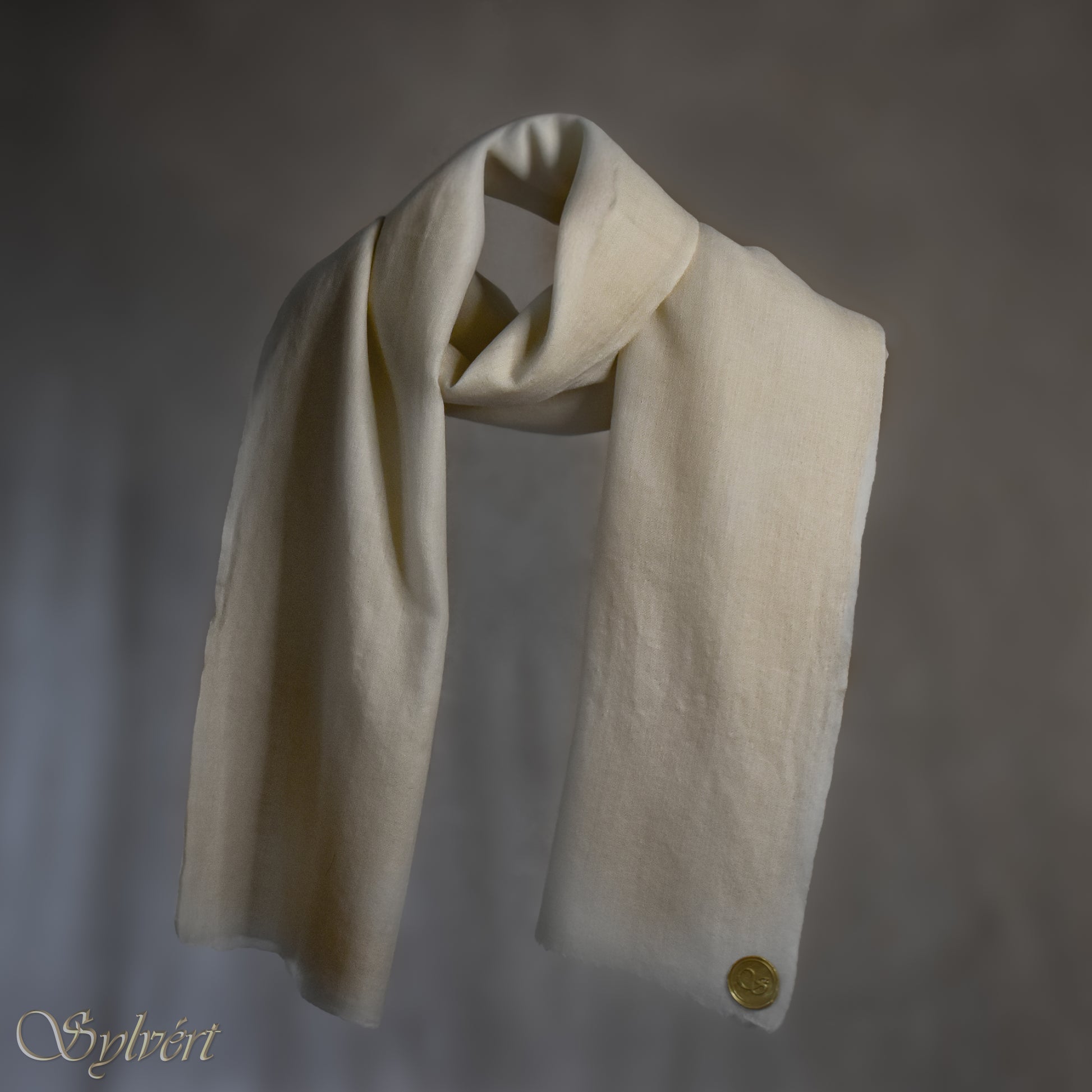 A white Corvella Orlien from Sylvért's Coronis collection, wrapped around itself, suspend in the air behind a beige background, displaying the gold Sylvért stamp