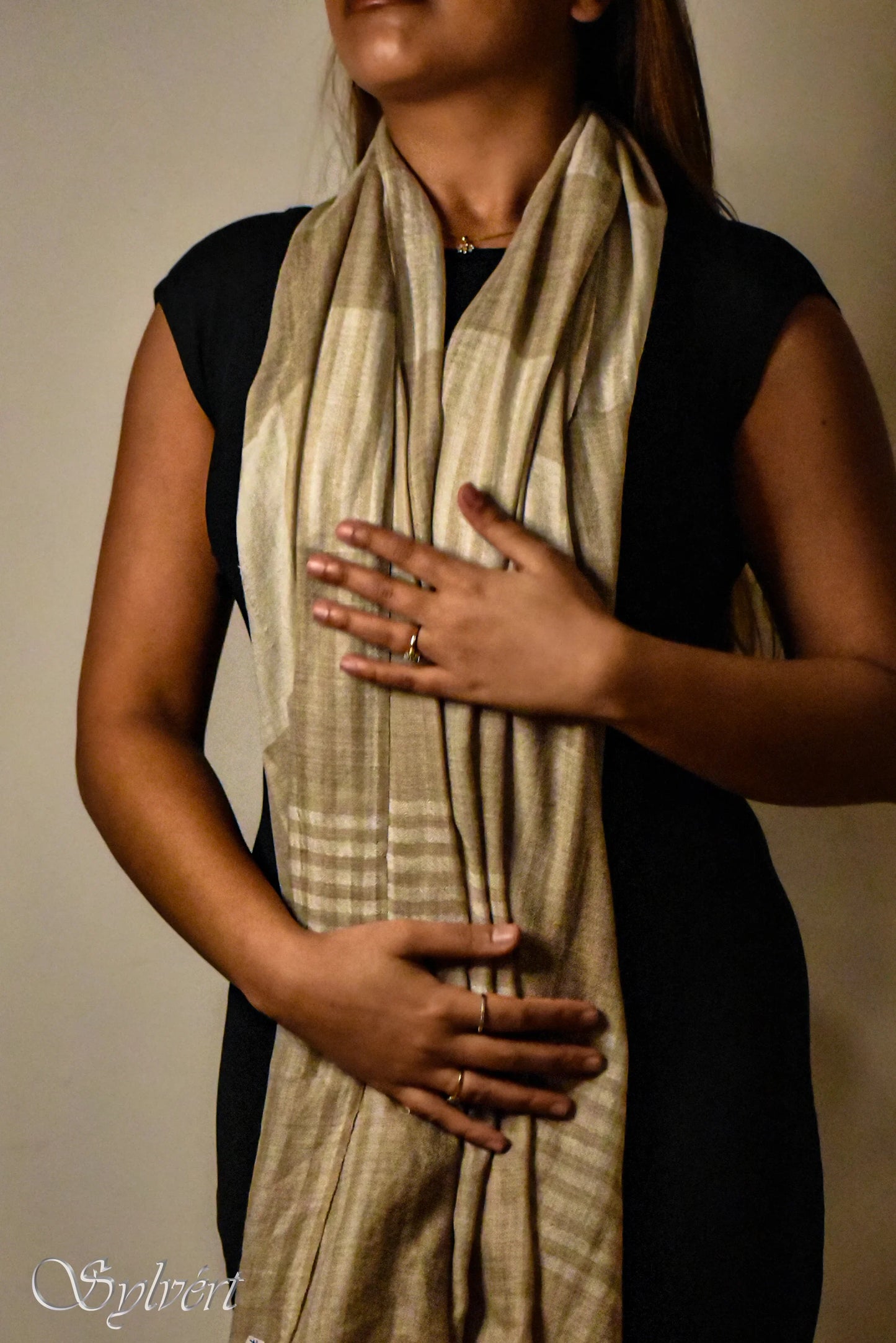 Woman wearing a beige striped scarf over a black dress, showcasing rings on her fingers