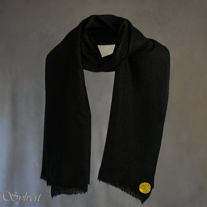 A black Corvella Noctra from Sylvért's Coronis collection, wrapped around itself, suspend in the air behind a beige background, displaying the gold Sylvért stamp
