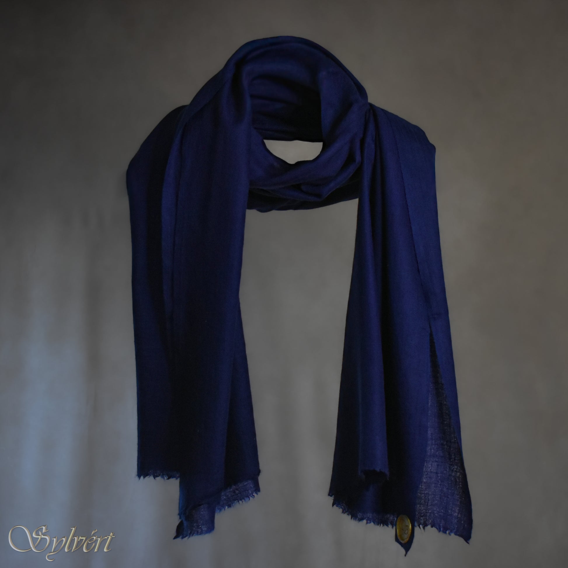 A blue Corvella Norien from Sylvért's Coronis collection, wrapped around itself, suspend in the air behind a beige background, displaying the gold Sylvért stamp