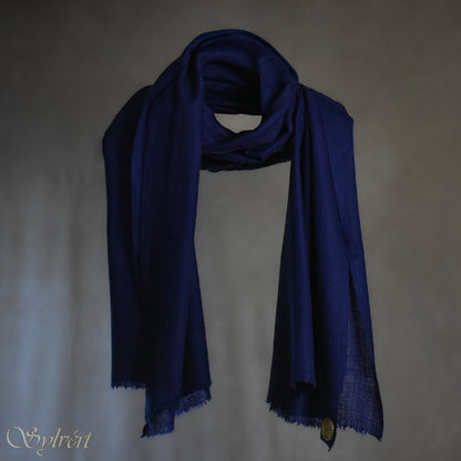 A blue Corvella Norien from Sylvért's Coronis collection, wrapped around itself, suspend in the air behind a beige background, displaying the gold Sylvért stamp