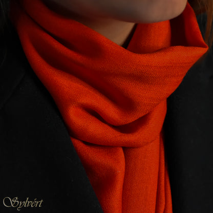 A styled shot of a red cashmere Rivella Sirel scarf from Sylvért's Rivanor collection worn under a black coat