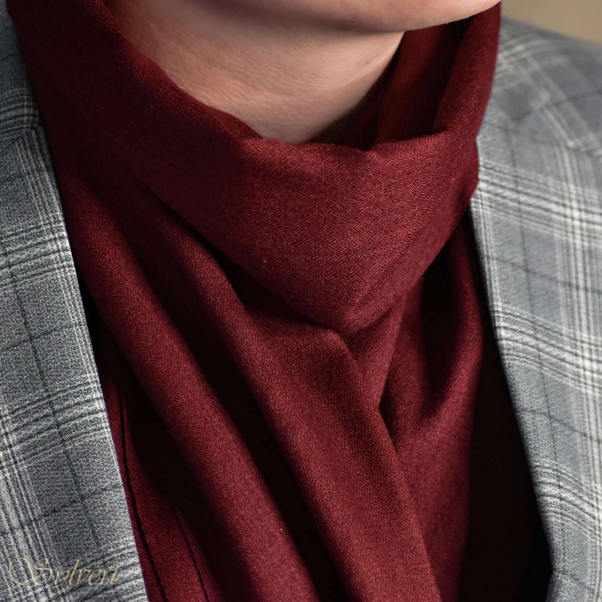 A styled shot of a maroon cashmere Rivella Morven scarf from Sylvért's Rivanor collection worn under a grey plaid blazer