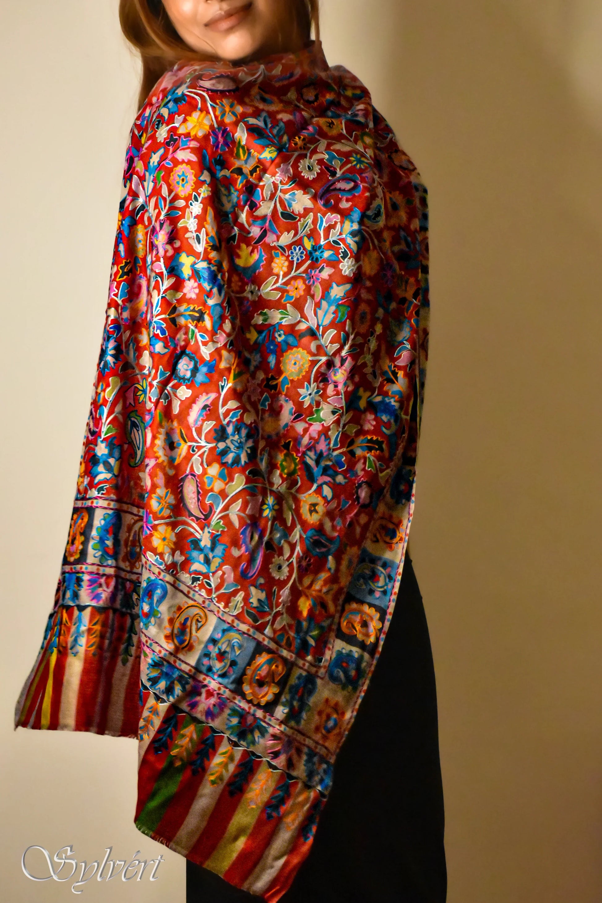 woman wearing vibrant red floral embroidered shawl with colorful paisley and stripe border