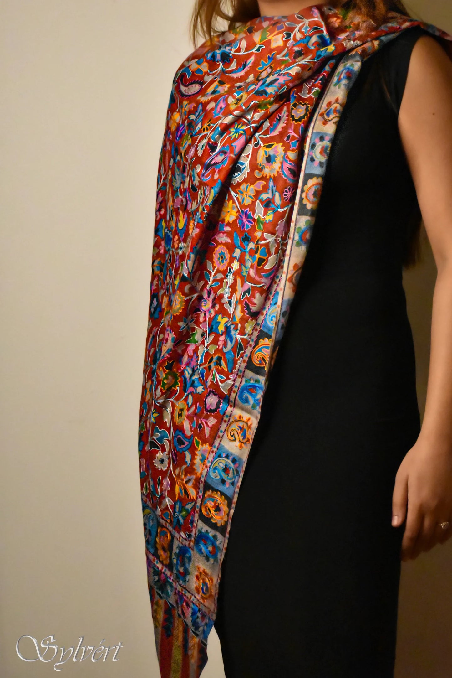 Woman wearing colorful embroidered floral shawl over black sleeveless dress against plain background
