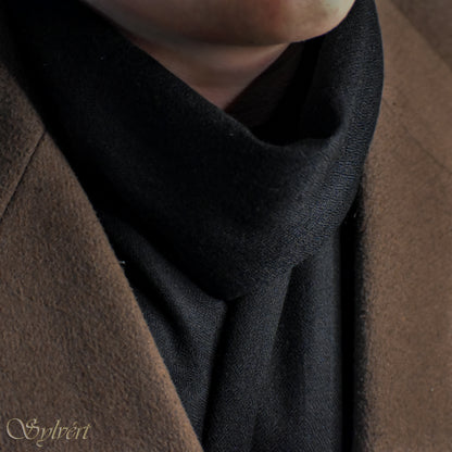 A styled shot of a black cashmere Rivella Velin scarf from Sylvért's Rivanor collection worn under a brown coat
