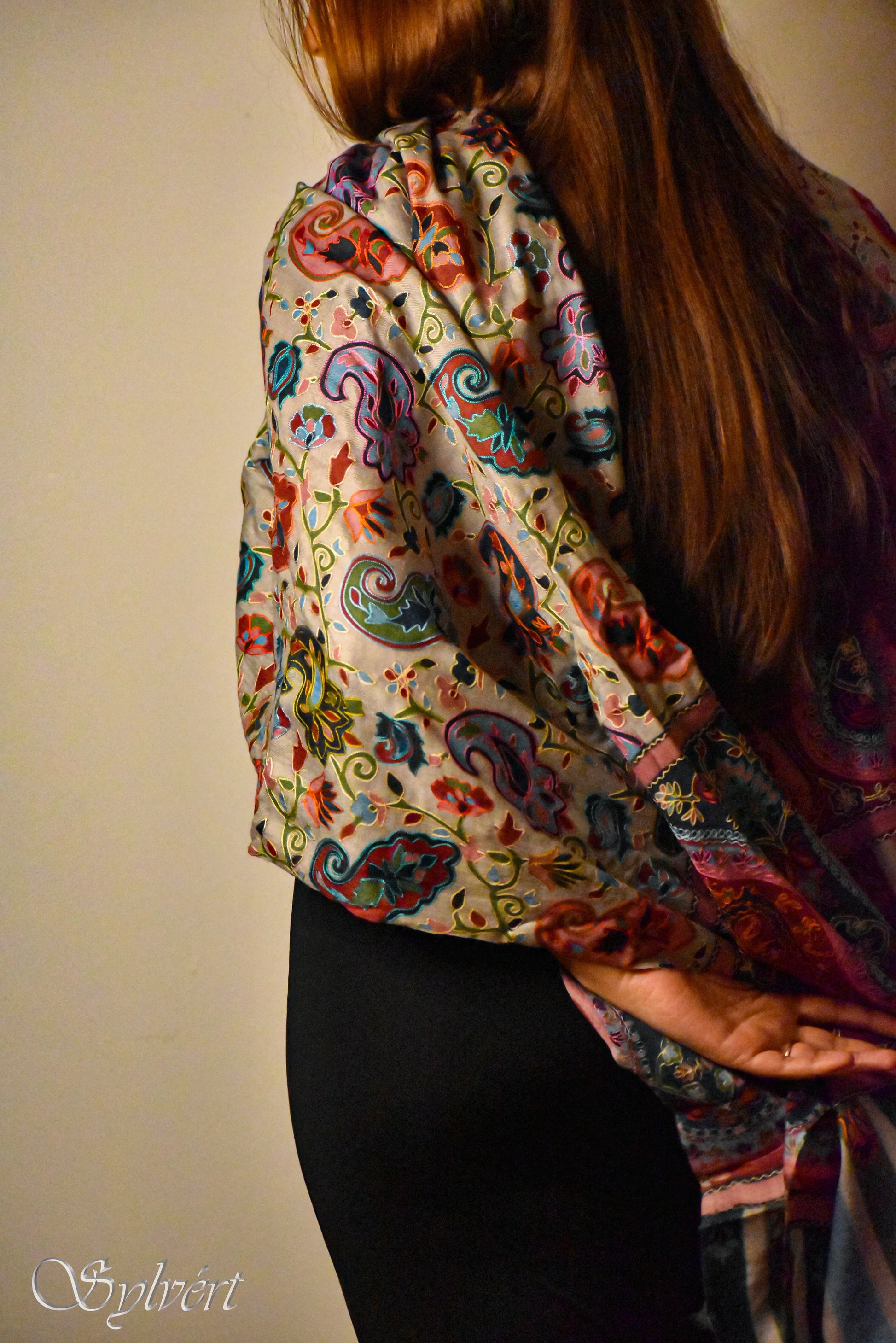 Woman with long brown hair wearing a vibrant paisley patterned shawl over black pants
