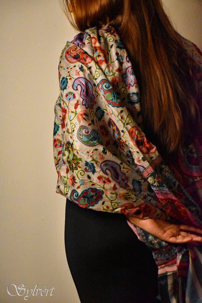 Woman with long brown hair wearing a vibrant paisley patterned shawl over black pants