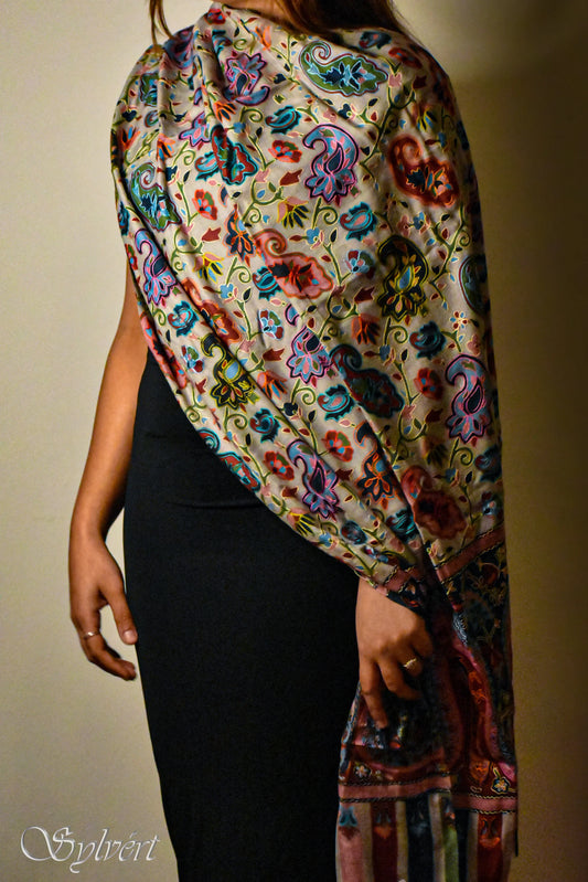 Woman wearing a colorful floral paisley shawl over a black dress against neutral background