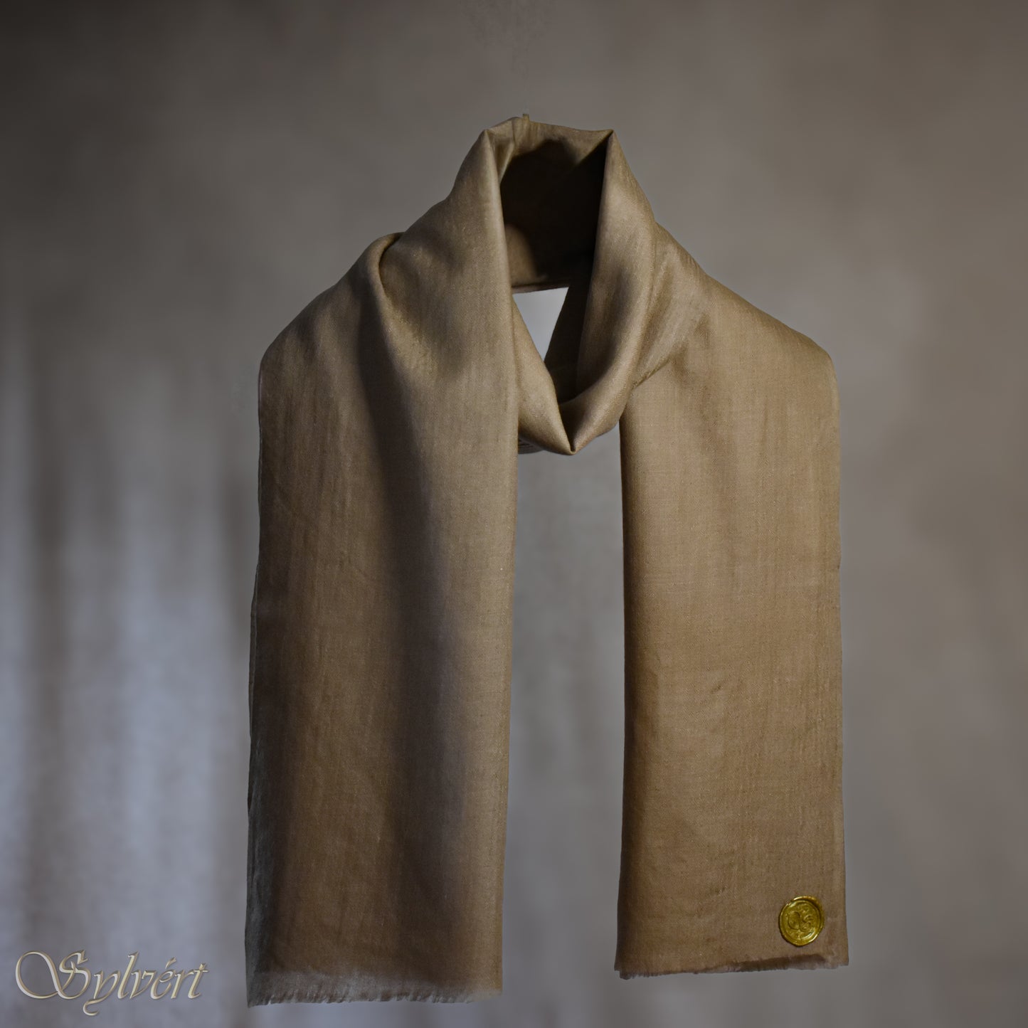 A beige Corvella Draván from Sylvért's Coronis collection, wrapped around itself, suspend in the air behind a beige background, displaying the gold Sylvért stamp