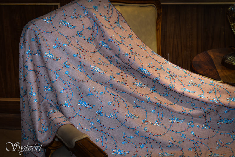 Draped product image of a beige Corvios handloomed pashmina stole with red, white and blue hand needle embroidery from Sylvért's Coronis collection